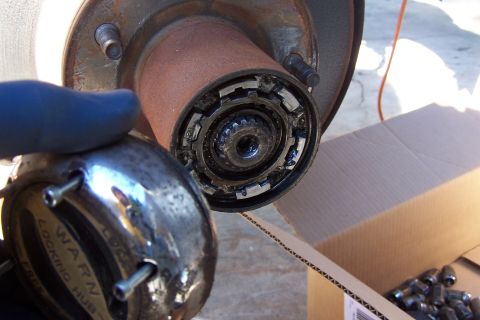 1990 Ford Bronco - A chrome locking hub, labeled "WARN LOCKING HUB", is held near a rusty wheel hub assembly.