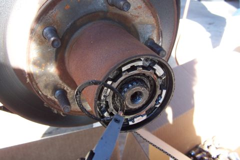 1990 Ford Bronco - Close-up of a vehicle's wheel hub assembly with a locking ring being removed by pliers.