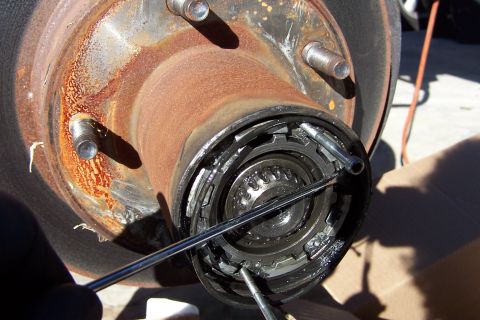 1990 Ford Bronco - Close-up of a rusty brake drum and wheel hub with exposed bearing being serviced outdoors.