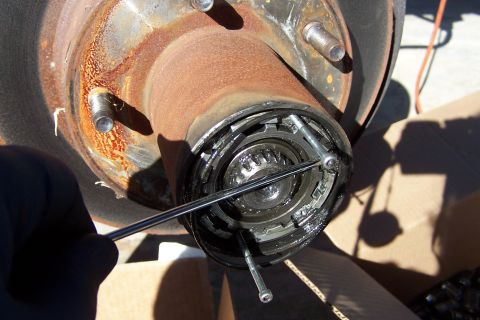 1990 Ford Bronco - A gloved hand uses tools to adjust the internal components of a vehicle's manual locking hub assembly.