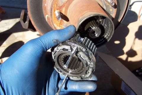 1990 Ford Bronco - A close-up view of a damaged manual locking hub, showing its internal gears and a gloved hand holding it.