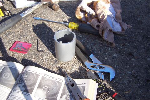 1990 Ford Bronco - Tools laid out on gravel, including a ball joint socket and a repair manual open to a diagram.
