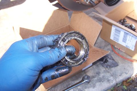 1990 Ford Bronco - A mechanic holds a heavily greased and worn wheel bearing, likely removed from a vehicle's axle assembly.
