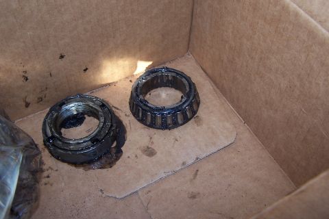 1990 Ford Bronco - Two automotive parts, a wheel bearing and a nut, are shown in a cardboard box, covered in grease.