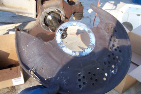 1990 Ford Bronco - A person is holding a removed brake dust shield next to a vehicle's hub assembly.