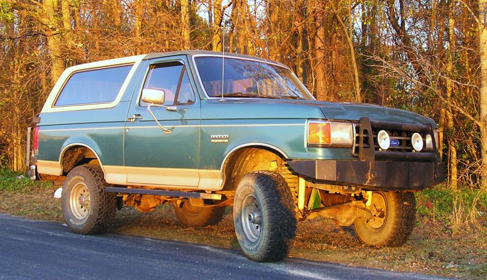 Lifted green Ford Bronco with white top and black brush guard at roadside