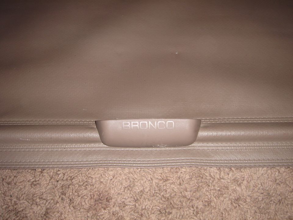 Close-up of a tan Ford Bronco cargo cover handle with 'BRONCO' embossed on it