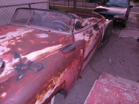 1986 Ford Bronco - This heavily rusted convertible appears to be undergoing restoration, with another vehicle parked nearby.
