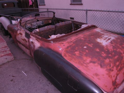 1986 Ford Bronco - A weathered red convertible sits next to a dark pickup truck, showing signs of extensive rust and disrepair.