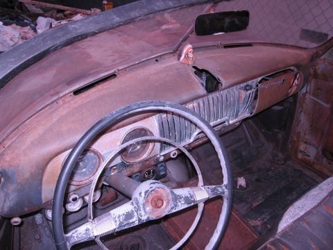 1986 Ford Bronco - Interior of a very old, rusted-out car, showing the dashboard and steering wheel.