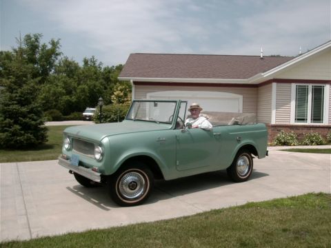 1993 Ford Bronco - A man in a hat drives a light green International Scout convertible in a driveway.