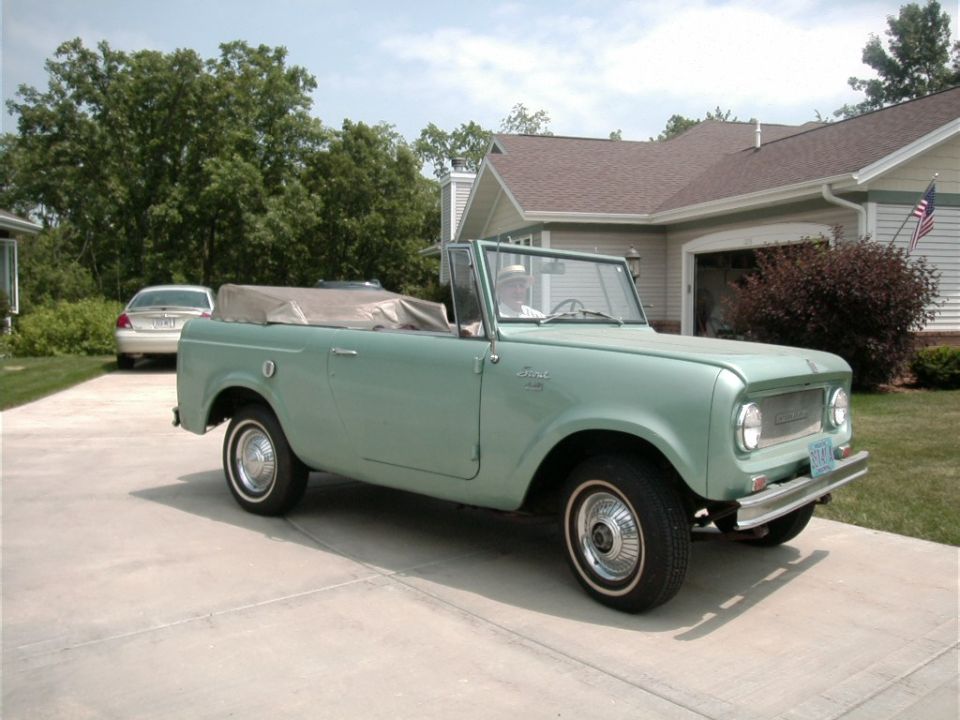 Mint green International Harvester Scout convertible parked in driveway. Another car is parked in the background
