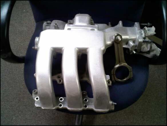 Silver aluminum intake manifold and connecting rod on a dark chair