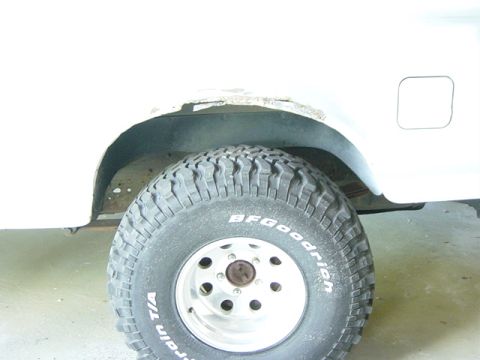 1993 Ford Bronco - Close-up of a white vehicle's rear wheel well with visible rust and a BFGoodrich All-Terrain T/A tire.