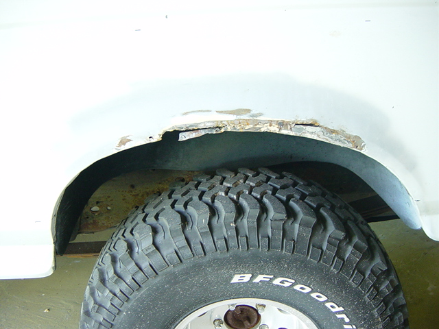 Close-up of a rusted wheel well and tire on a white vehicle. "BFGoodrich" text visible on tire