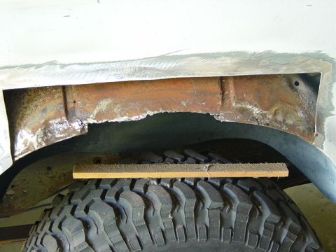 1993 Ford Bronco - Close-up of a heavily rusted wheel well with a piece of wood resting on the tire.