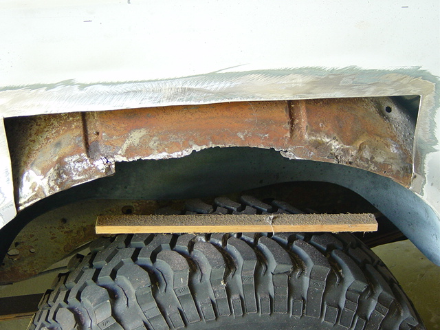 rusted wheel well with a piece of wood on top of a tire