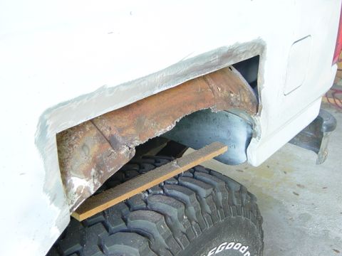 1993 Ford Bronco - Rust damage is visible in the rear wheel well of a white vehicle, with body filler applied to the exterior panel.