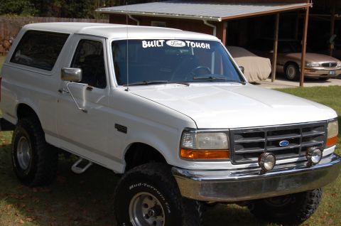 1993 Ford Bronco - A white Ford Bronco is parked in front of a house with another vehicle covered in a tarp in the background.