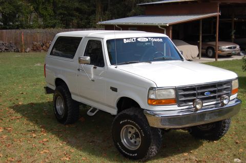 1993 Ford Bronco - This lifted white Ford Bronco features an aftermarket "Built Ford Tough" decal on its windshield and is parked on a grassy lawn.