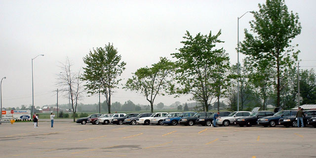 Several police cars parked in a lot, some with hoods up. Two people stand near the front