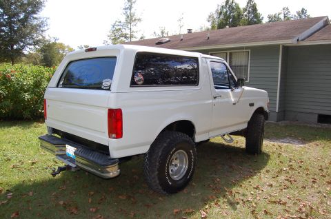 1993 Ford Bronco - A white Ford Bronco with a camper shell is parked on a grassy lawn next to a house on a sunny day.