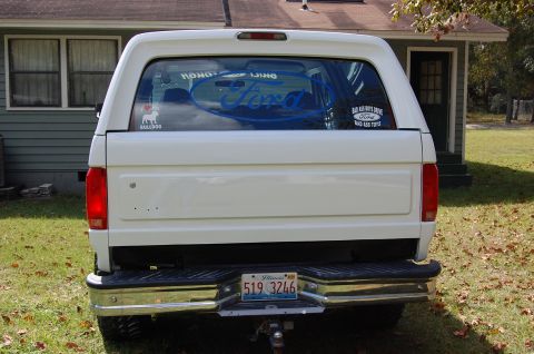 1993 Ford Bronco - Rear view of a white Ford Bronco with a camper shell and various stickers on the rear window.