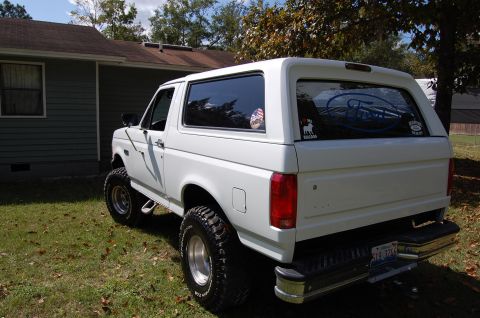 1993 Ford Bronco - White Ford Bronco with aftermarket wheels and tires, parked in a grassy yard near a house.