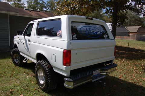 1993 Ford Bronco - This lifted white Ford Bronco is parked in a yard with a house and trees in the background.