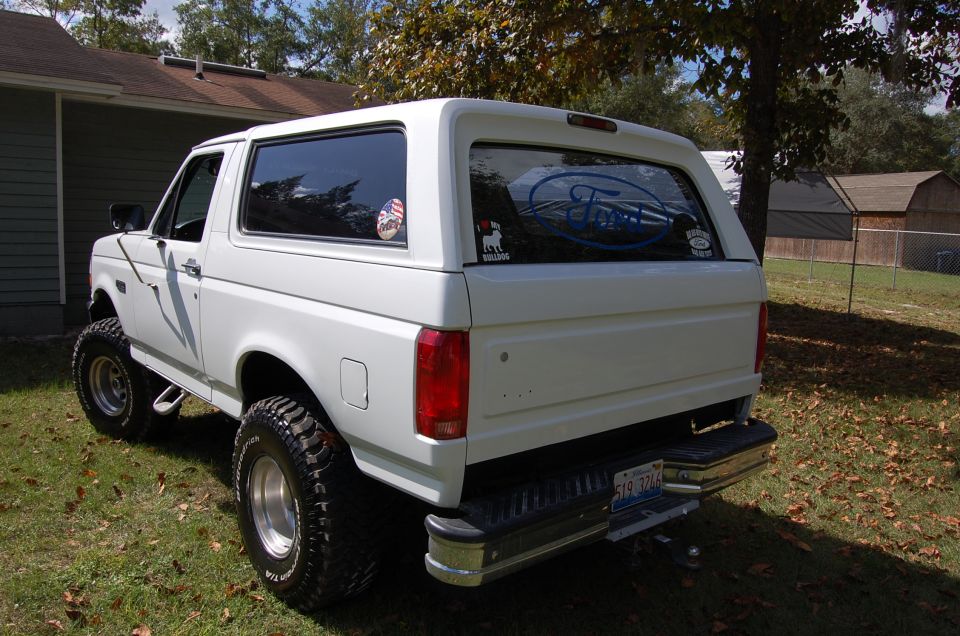 White Ford Bronco, lifted with large tires, parked in a grassy yard