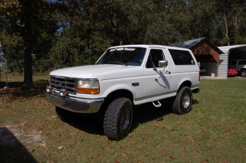 1993 Ford Bronco - A white 1993 Ford Bronco is parked on a grassy lawn with trees in the background.