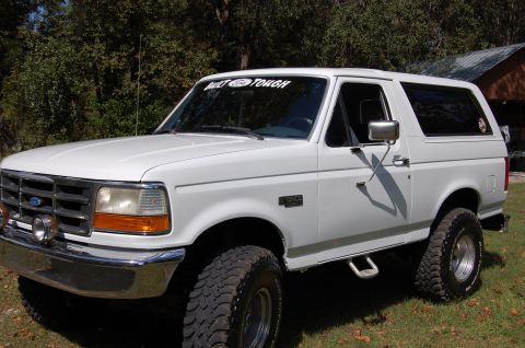 1993 Ford Bronco - White Ford Bronco SUV with "BUILT FORD TOUGH" banner and large off-road tires.