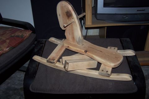 1990 Ford Bronco - A handmade wooden rocking horse is shown on a dark upholstered surface, with a television visible in the background.