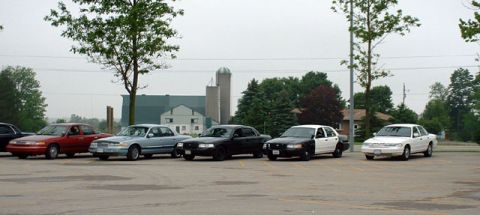 2000 Ford Crown Victoria - Several Ford Crown Victoria sedans and police cars are parked in a lot on an overcast day.