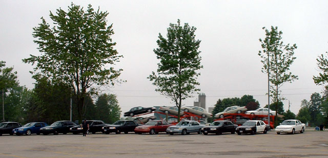Parked cars in a lot with a loaded two-level car-hauler trailer behind them