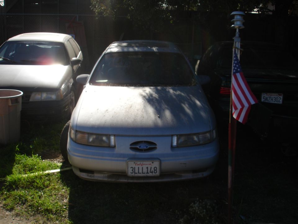 Dusty silver sedan parked outdoors with an American flag in front of another car.