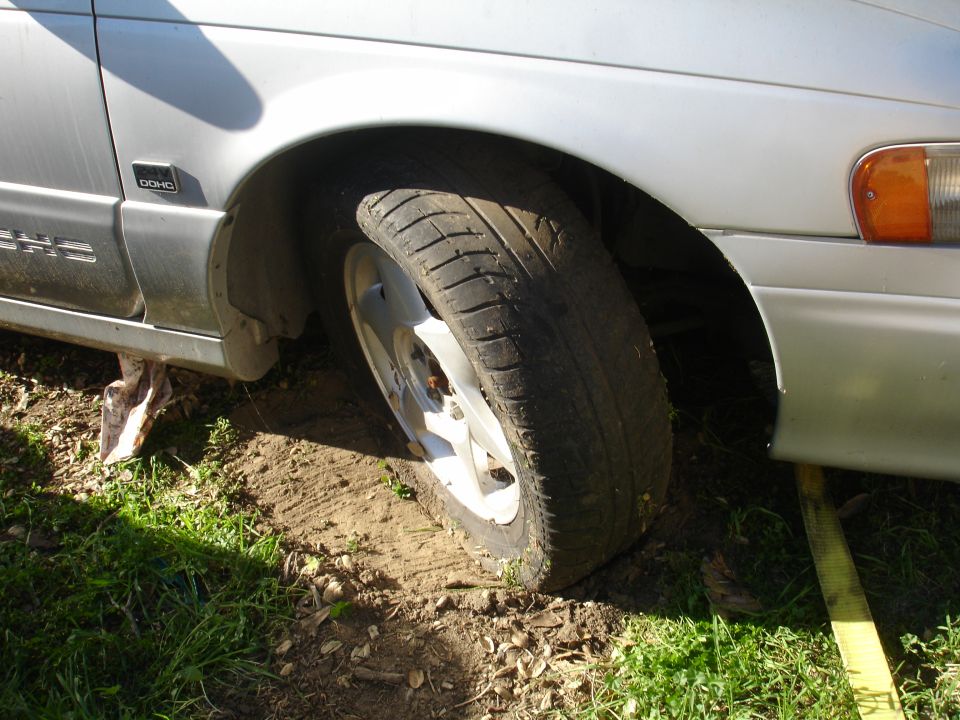 Silver sedan front passenger side tire stuck in dirt, yellow tow strap visible.
