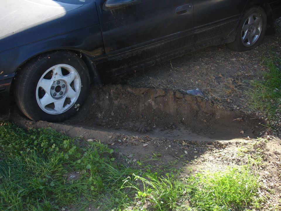 Black sedan stuck in a muddy ditch with front tire in the mud.