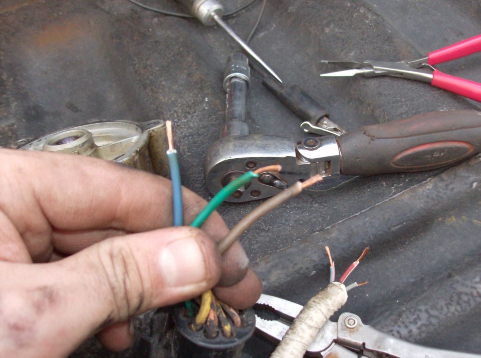 Close-up of a hand holding stripped electrical wires with tools in the background.