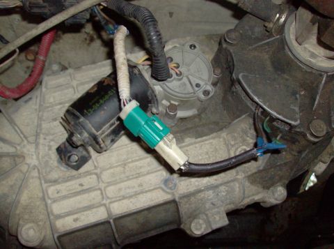1989 Ford Bronco - A close-up view shows a black transfer case actuator with a white and green electrical connector attached. The actuator has part number 13-…