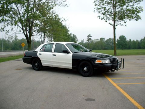 2000 Ford Crown Victoria - A two-tone police car is parked in a lot, showing its front and side profile.