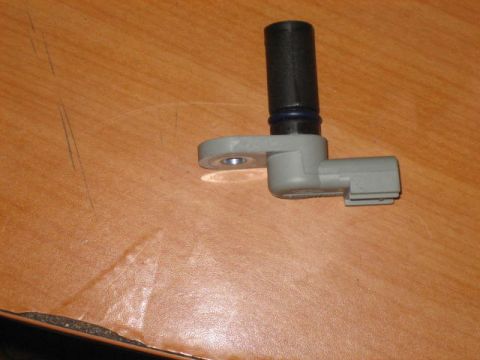 1996 Ford Thunderbird - A gray and black automotive sensor with a blue ring is shown resting on a wooden surface. The sensor has a rectangular mounting bracket and…