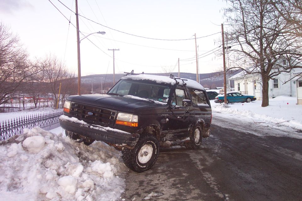 Black 1992 Ford Bronco stuck in a snow pile on a street in winter.