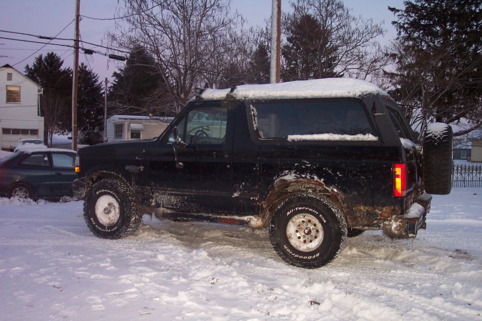 Black Ford Bronco in the snow with off-road tires and spare tire on the back.