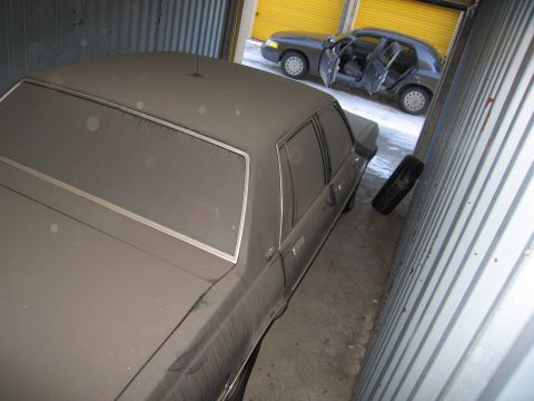 1991 Ford LTD Crown Victoria - Photograph of a dust-covered stored sedan in a metal storage unit, not a technical document.