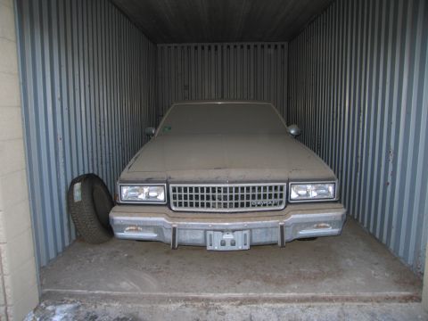 1991 Ford LTD Crown Victoria - Photograph of the front of a dust-covered Chevrolet sedan in storage, not a technical document.