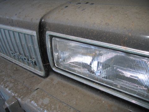 1991 Ford LTD Crown Victoria - Photograph of a Chevrolet headlight, grille, and dusty fender, not a technical document.