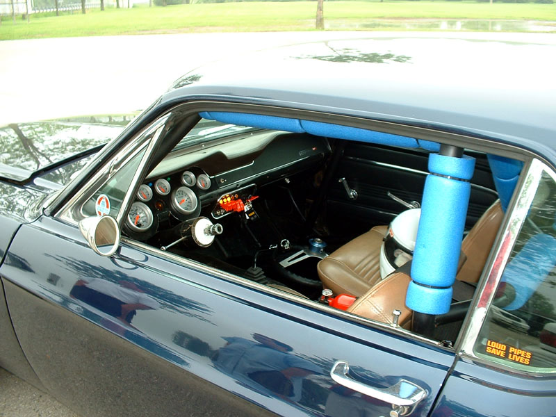 Interior view of a dark blue classic car with a roll cage, racing seats, and many gauges on the dashboard