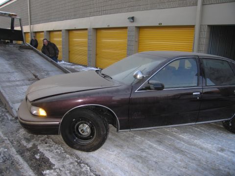 1991 Ford LTD Crown Victoria - Front three-quarter photo of a dark Chevrolet Caprice sedan being winched onto a flatbed tow truck in a snowy storage lot.