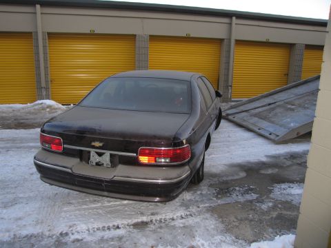 1991 Ford LTD Crown Victoria - Rear photo of a dark Chevrolet Caprice sedan in a snowy storage lot beside a flatbed tow ramp.
